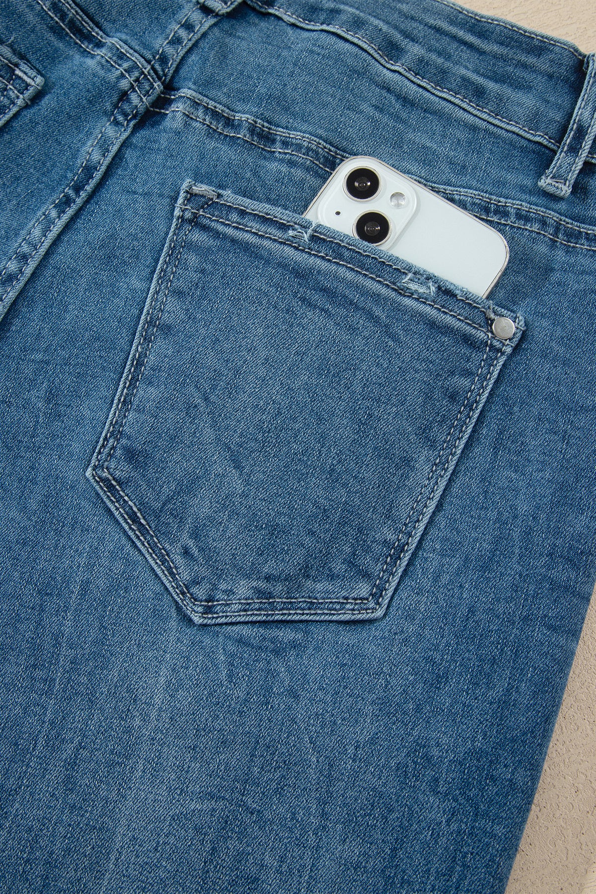 Jean flare taille haute bleu moyen, poche avant et surpiqûres, téléphone visible.
