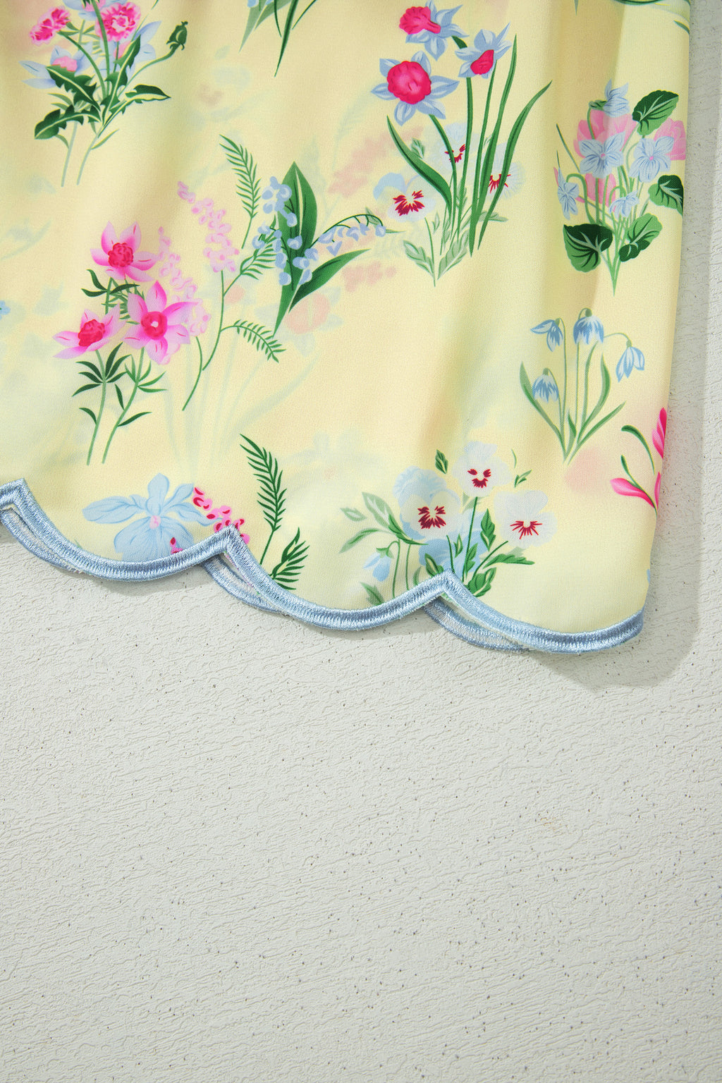Ourlet festonné avec bordure bleu clair et fleurs multicolores sur robe crème.