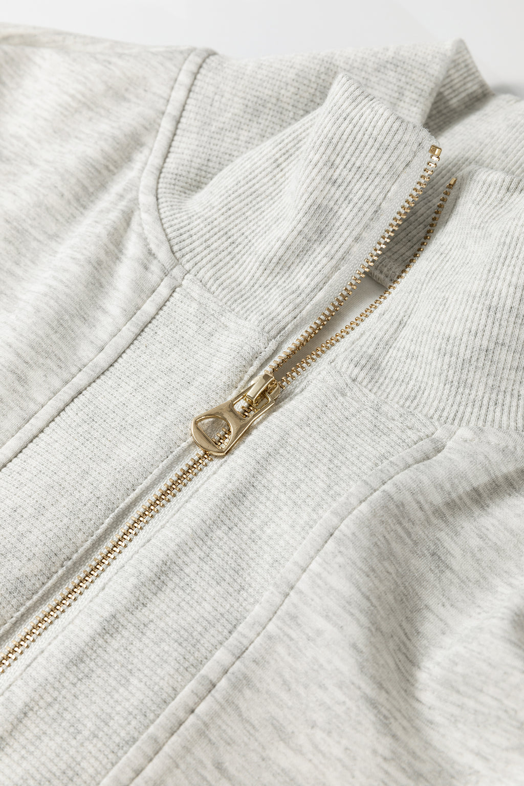 Détail ensemble : fermeture zippée dorée sur polo en tissu gris clair