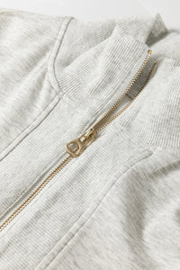 Détail ensemble : fermeture zippée dorée sur polo en tissu gris clair