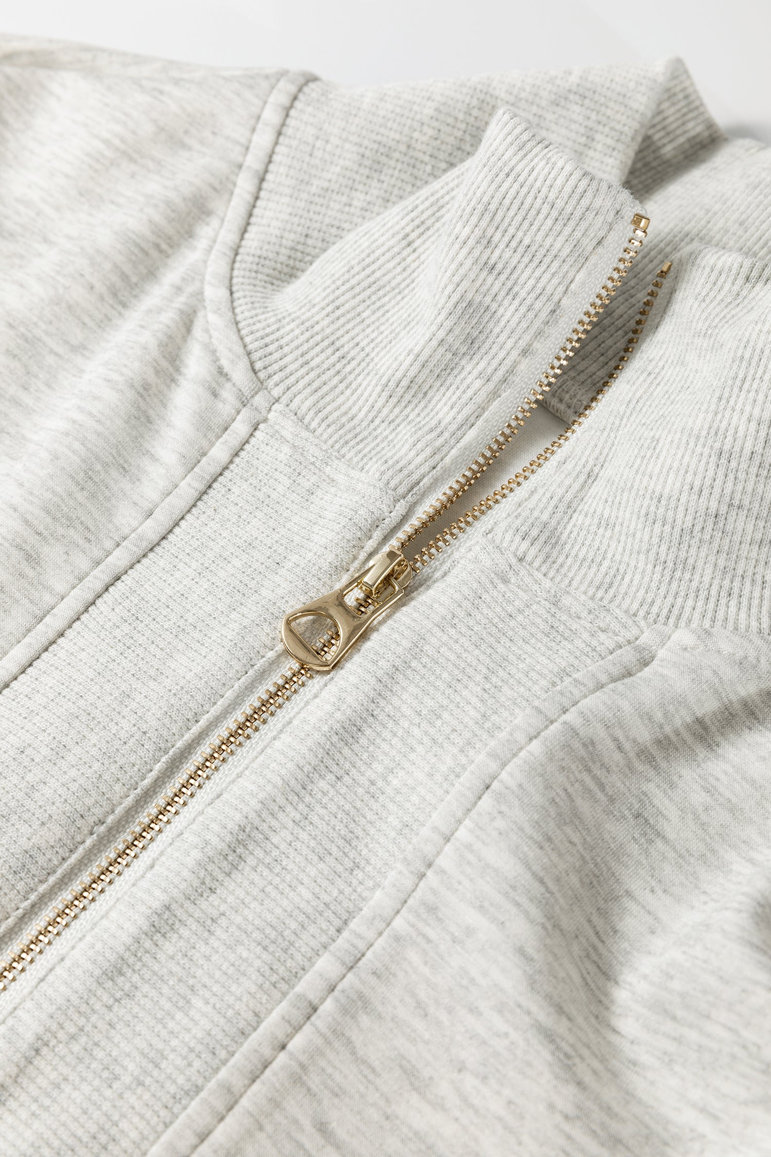 Détail ensemble : fermeture zippée dorée sur polo en tissu gris clair