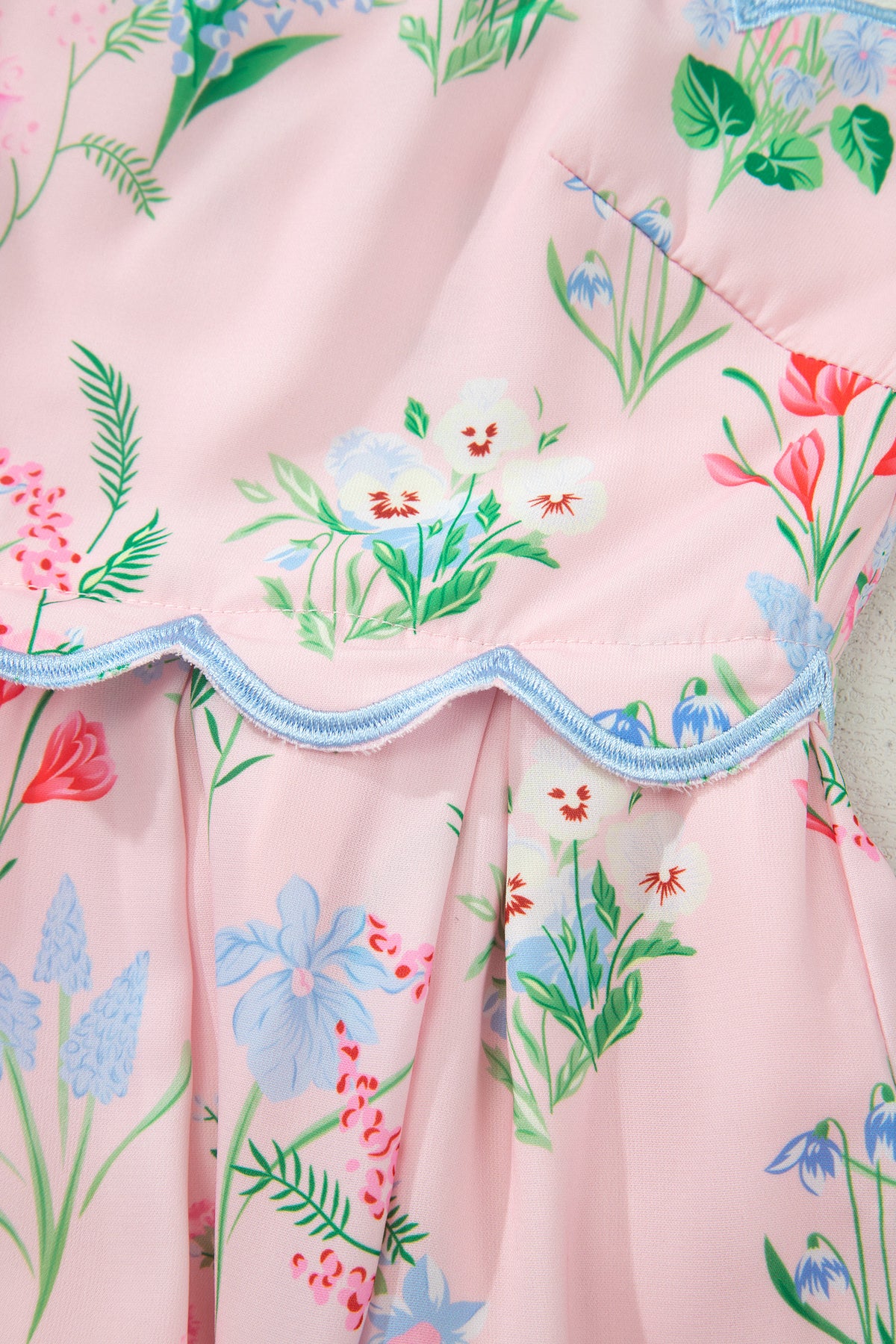 Robe rose à fleurs, volant ondulé avec bord bleu, plis froncés.