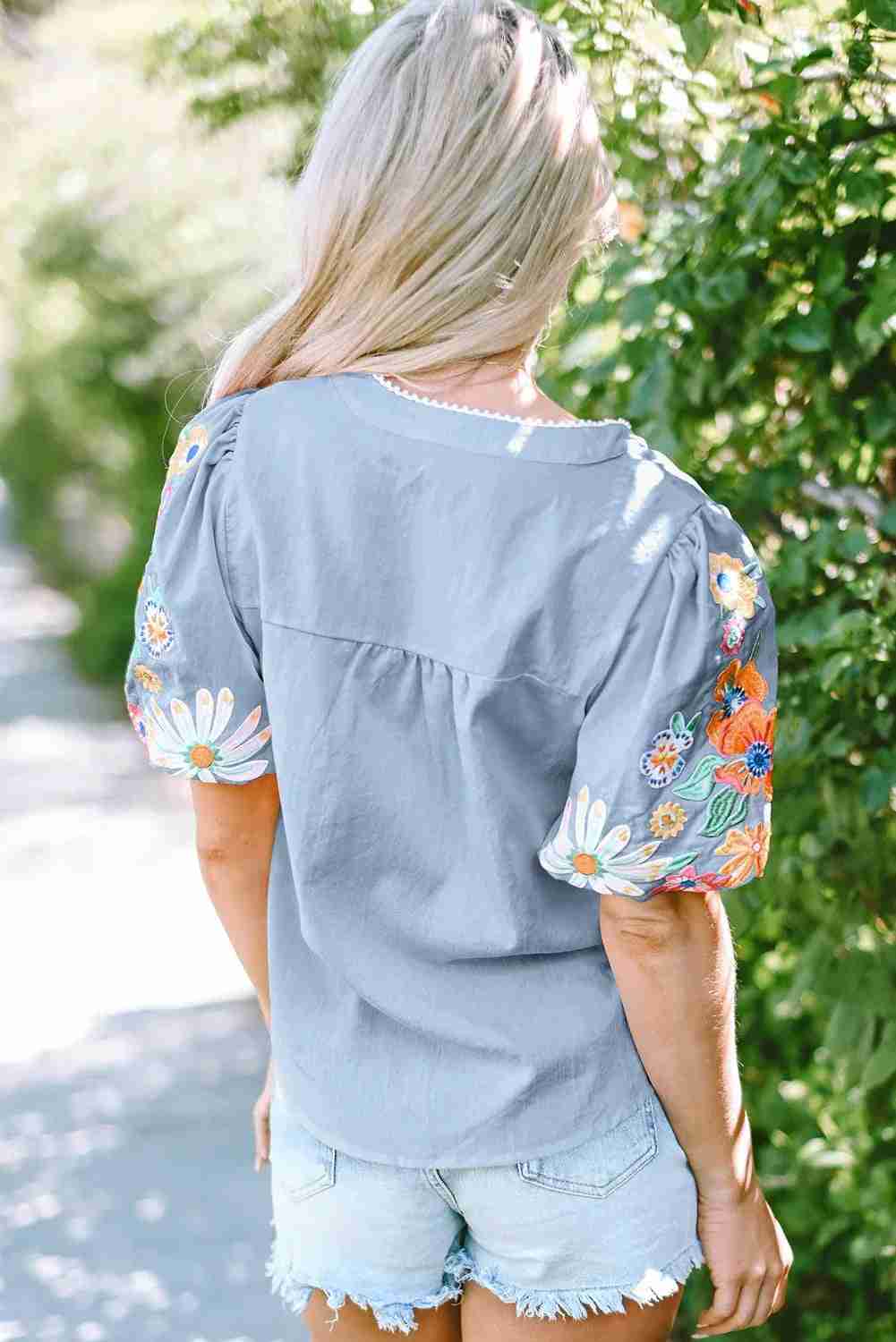 Chemisier femme gris à broderies florales multicolores au dos, manches courtes bouffantes.