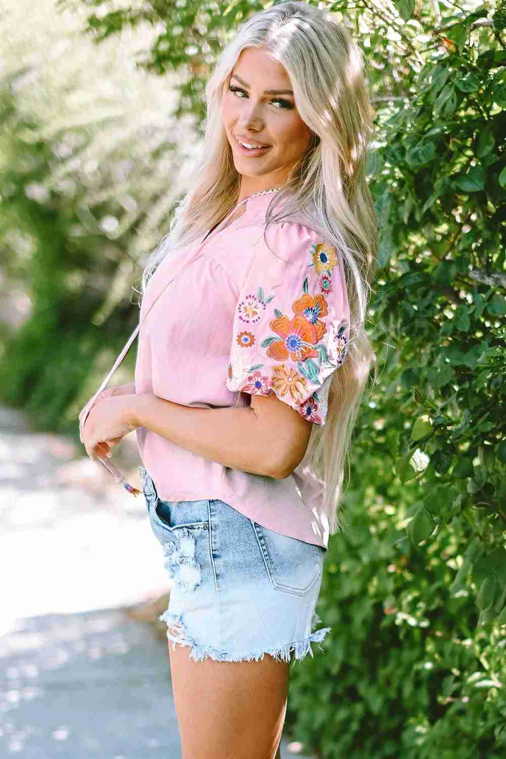 Chemisier femme rose avec broderies florales multicolores sur les manches courtes.