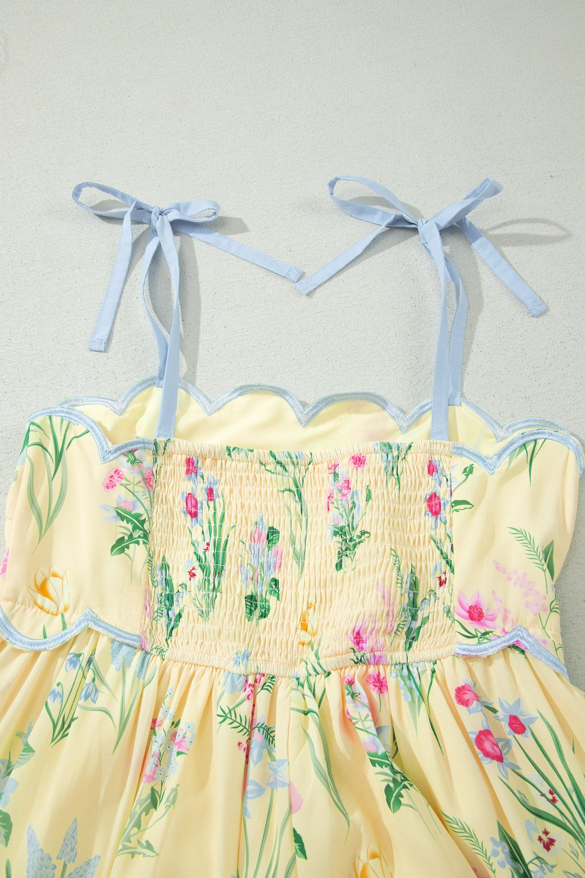 Haut de robe crème : bretelles nouées bleu clair, smock fleuri et ourlet festonné.