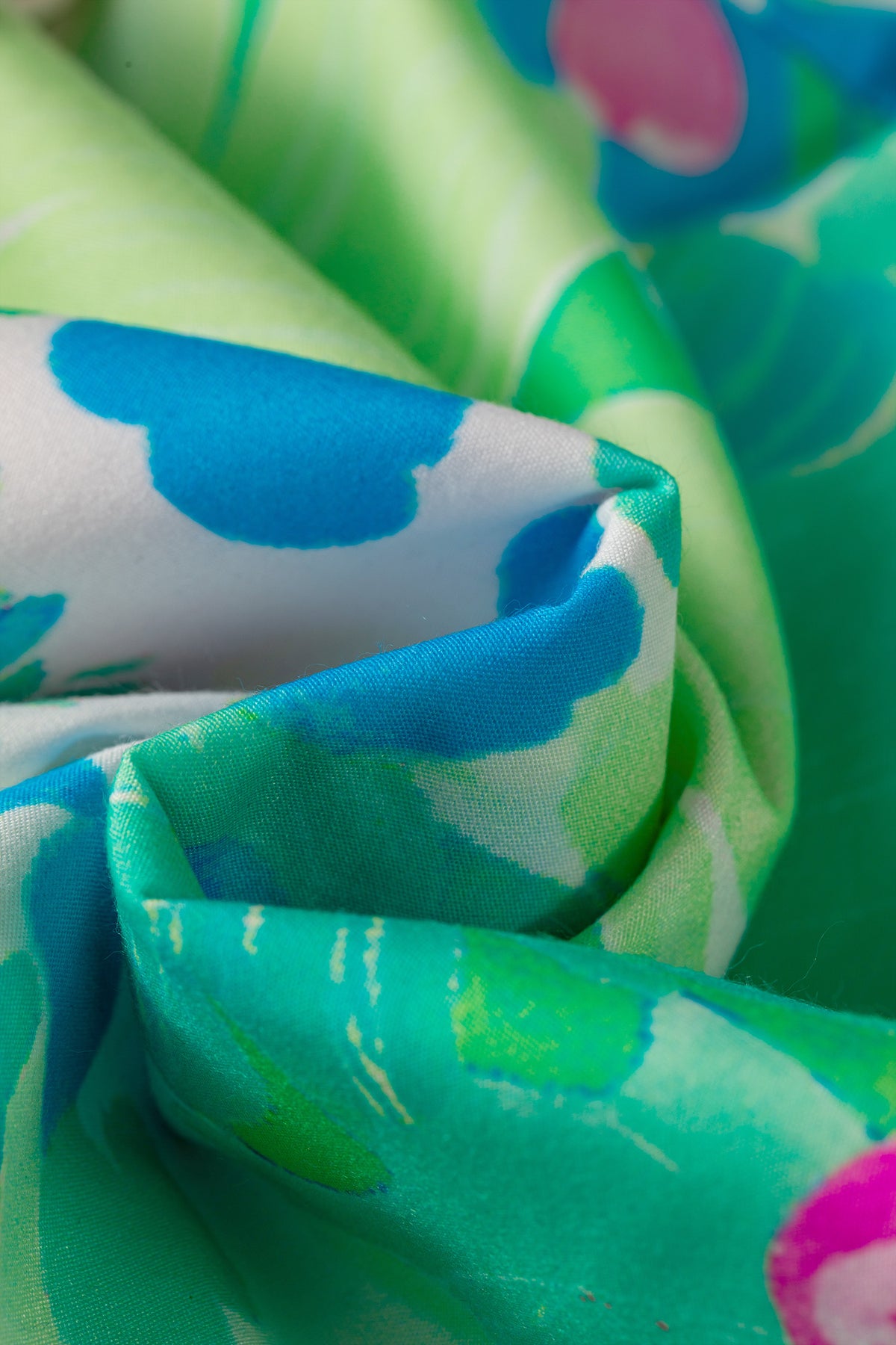 Tissu de robe vert clair avec motifs bleus et touches roses, vue rapprochée.