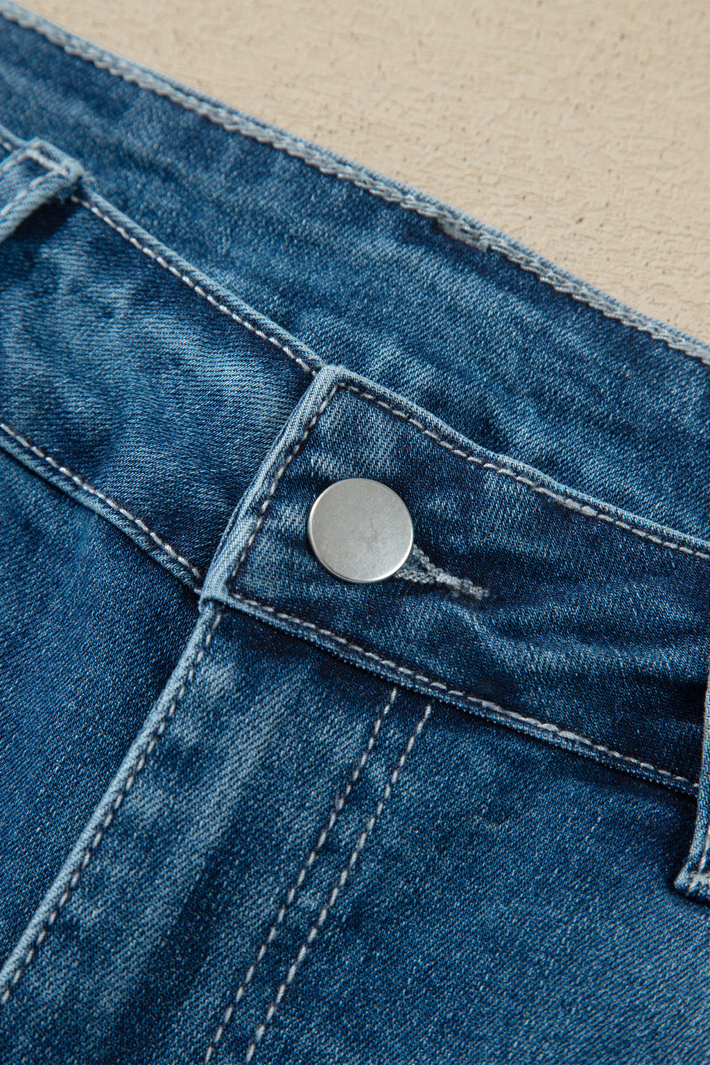 Détail fermeture jean flare taille haute bleu moyen, bouton métal et surpiqûres.