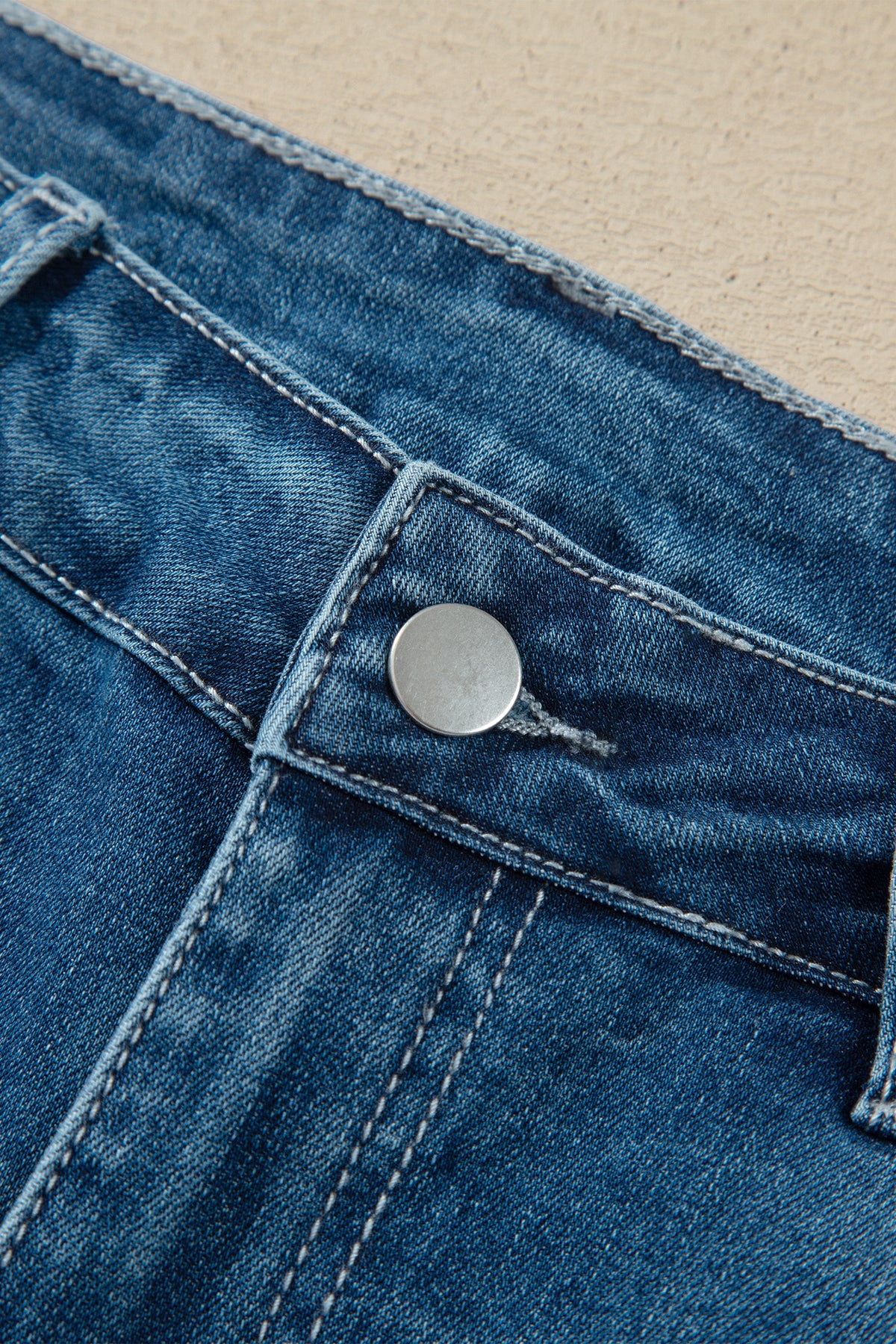 Détail fermeture jean flare taille haute bleu moyen, bouton métal et surpiqûres.