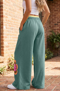 Pantalon ample vert mer, fleurs colorées sur la jambe, taille élastique à cordon, coupe large.