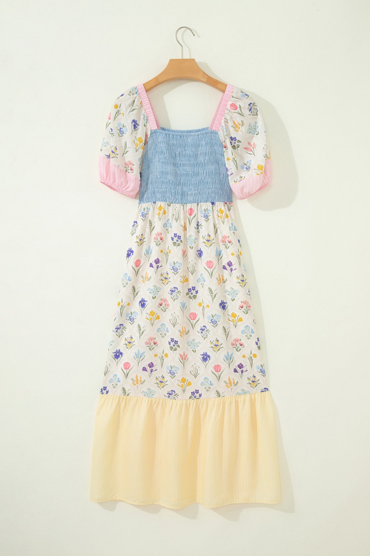 Robe longue sur cintre: buste bleu smocké, jupe fleurie, ourlet volanté crème, manches roses.