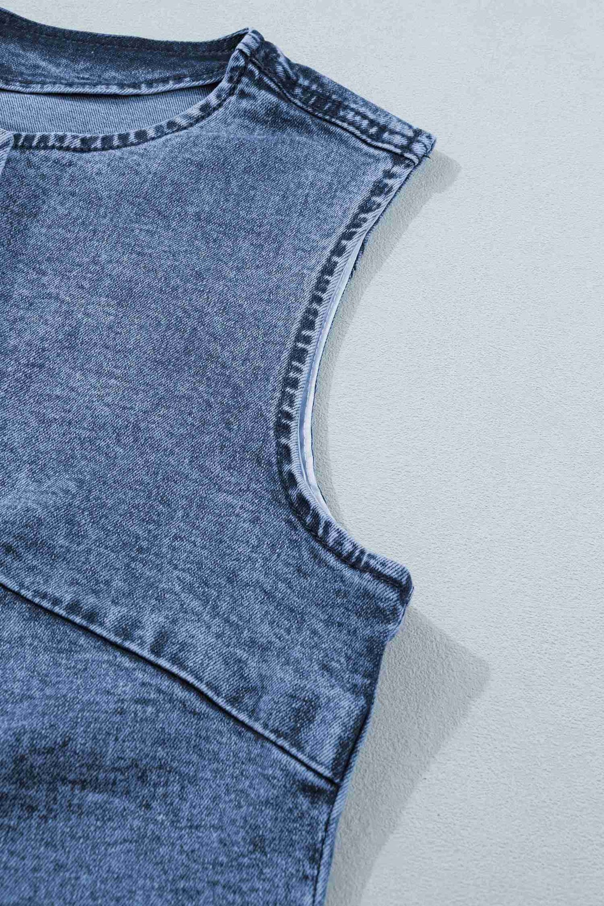 Encolure et emmanchure du gilet en denim bleu sans manches, surpiqûres visibles