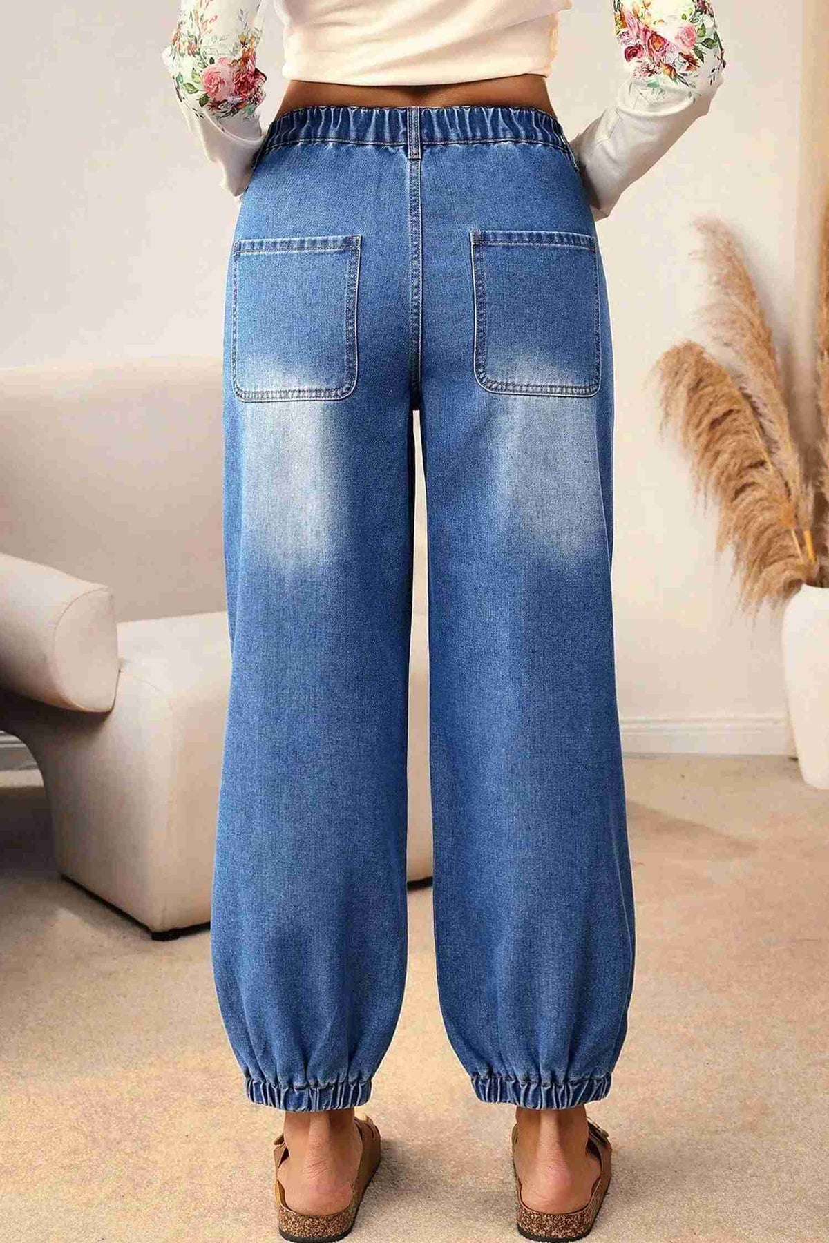 Jean bleu taille haute fuselé, poches arrière, bas resserré, surpiqûres visibles.