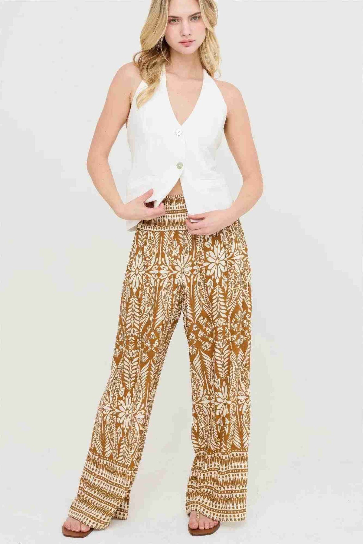 Pantalon fluide ocre à motifs floraux blancs, taille smockée, coupe ample et longue.