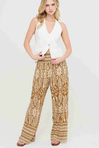 Pantalon fluide ocre à motifs floraux blancs, taille smockée, coupe ample et longue.