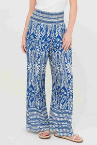 Pantalon fluide bleu à motifs fleuris blancs, taille smockée, bas évasé et rayé.
