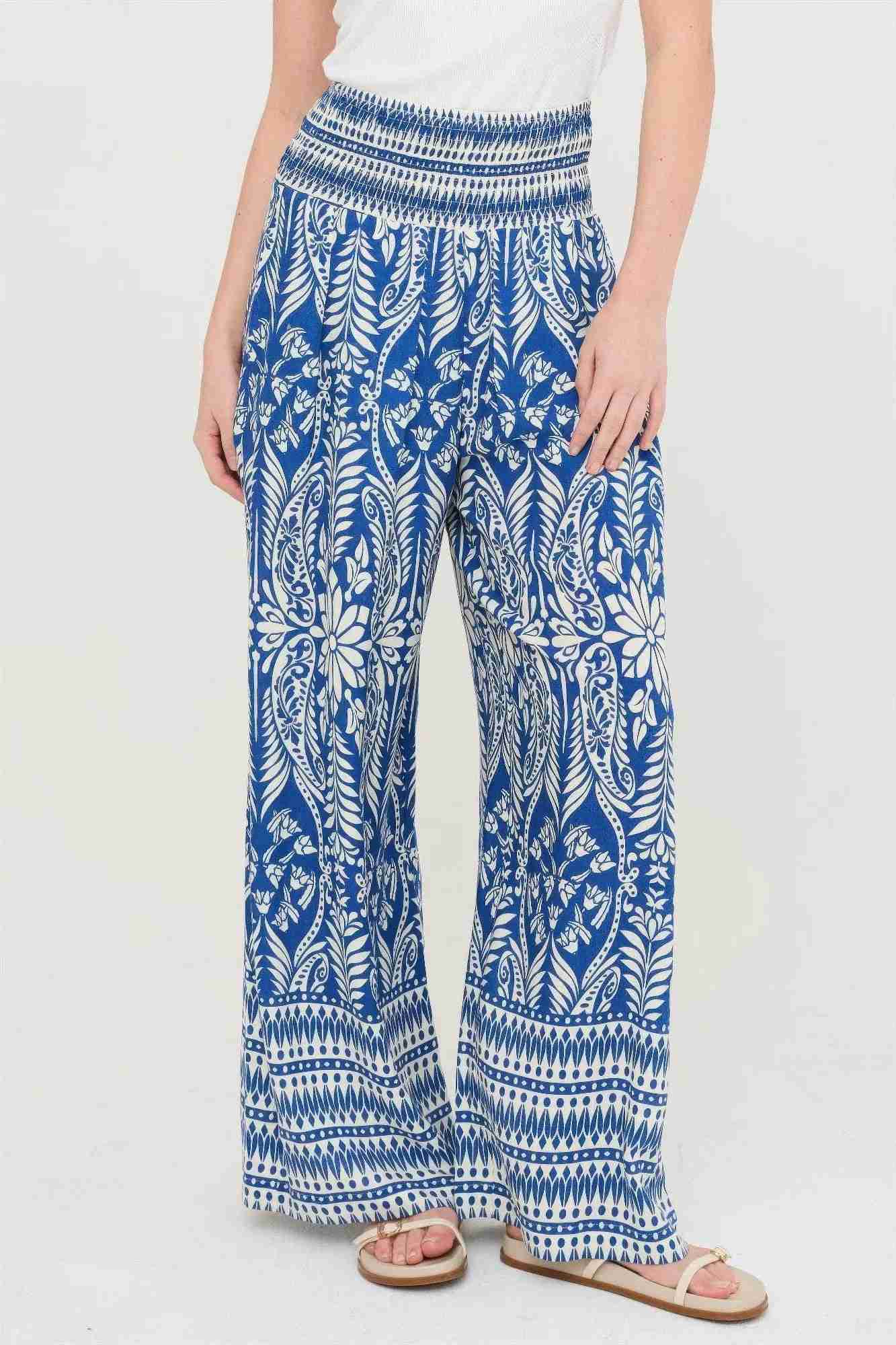 Pantalon fluide bleu à motifs fleuris blancs, taille smockée, bas évasé et rayé.
