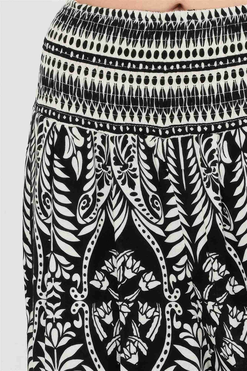 Pantalon noir à motif végétal blanc, taille smockée et ourlet à rayures contrastées.