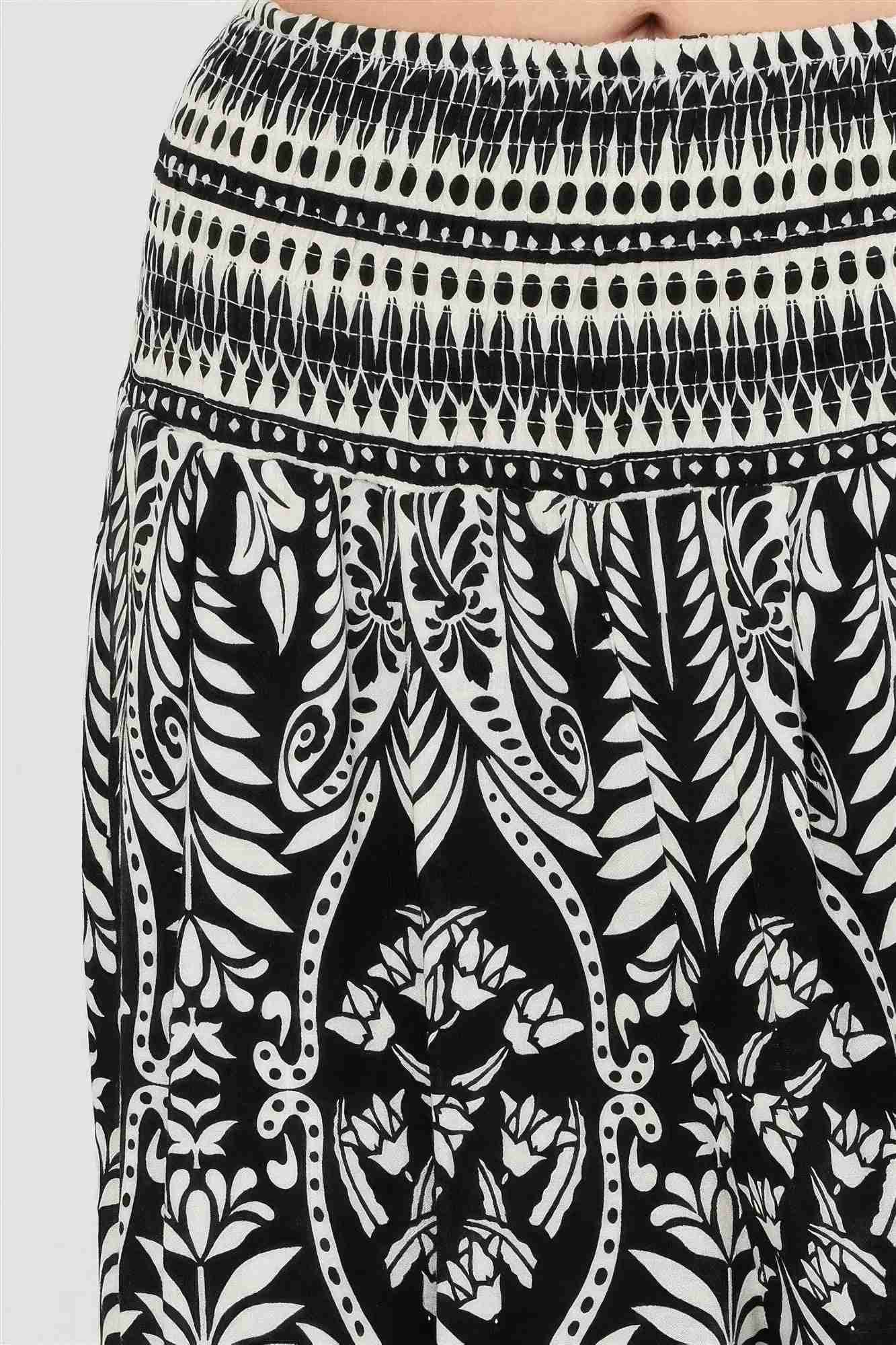 Pantalon noir à motif végétal blanc, taille smockée et ourlet à rayures contrastées.