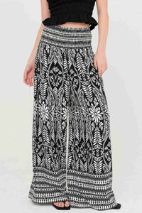 Pantalon fluide noir à motif fleuri blanc, taille smockée élastique, jambes évasées.