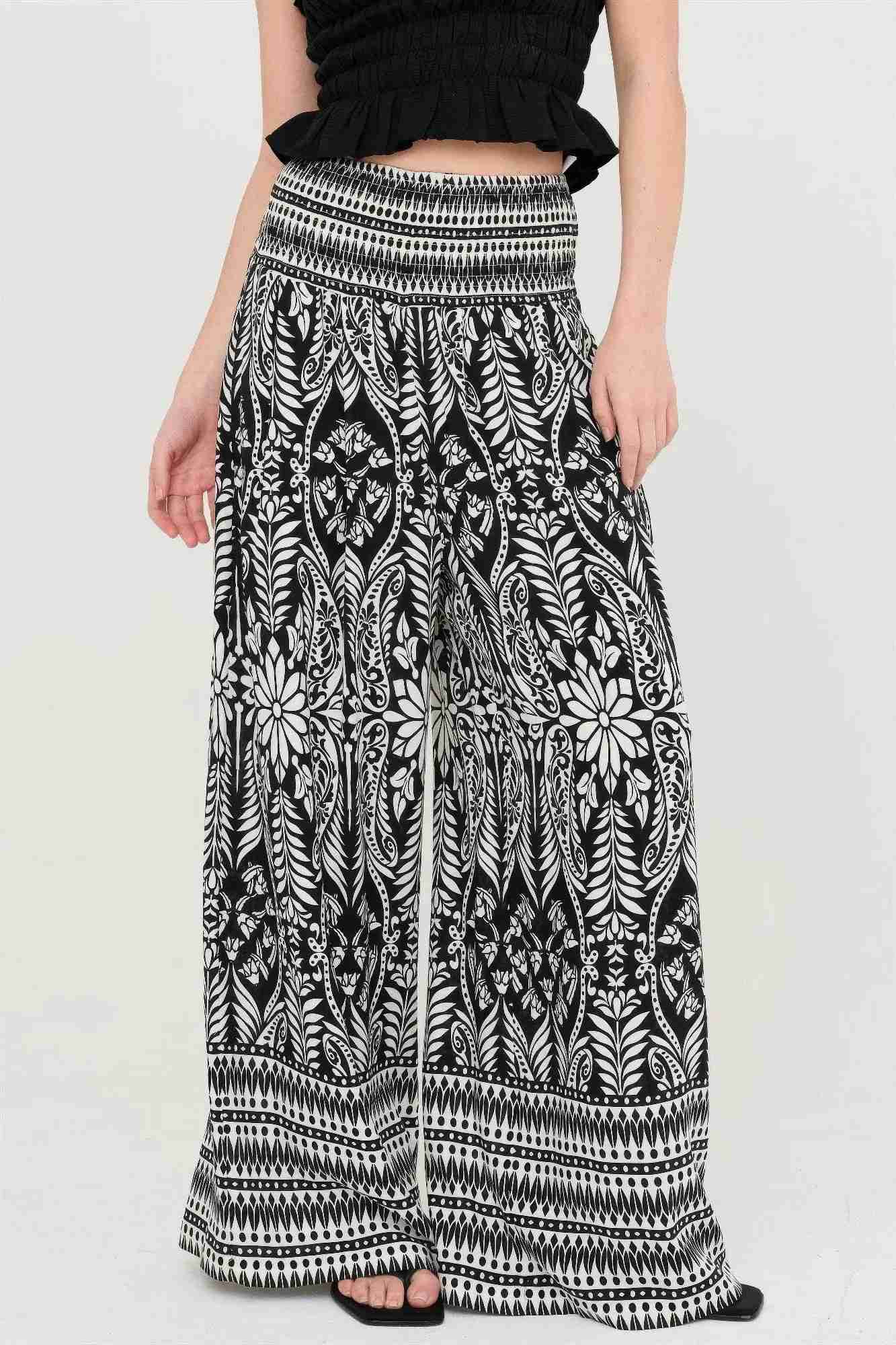 Pantalon fluide noir à motif fleuri blanc, taille smockée élastique, jambes évasées.