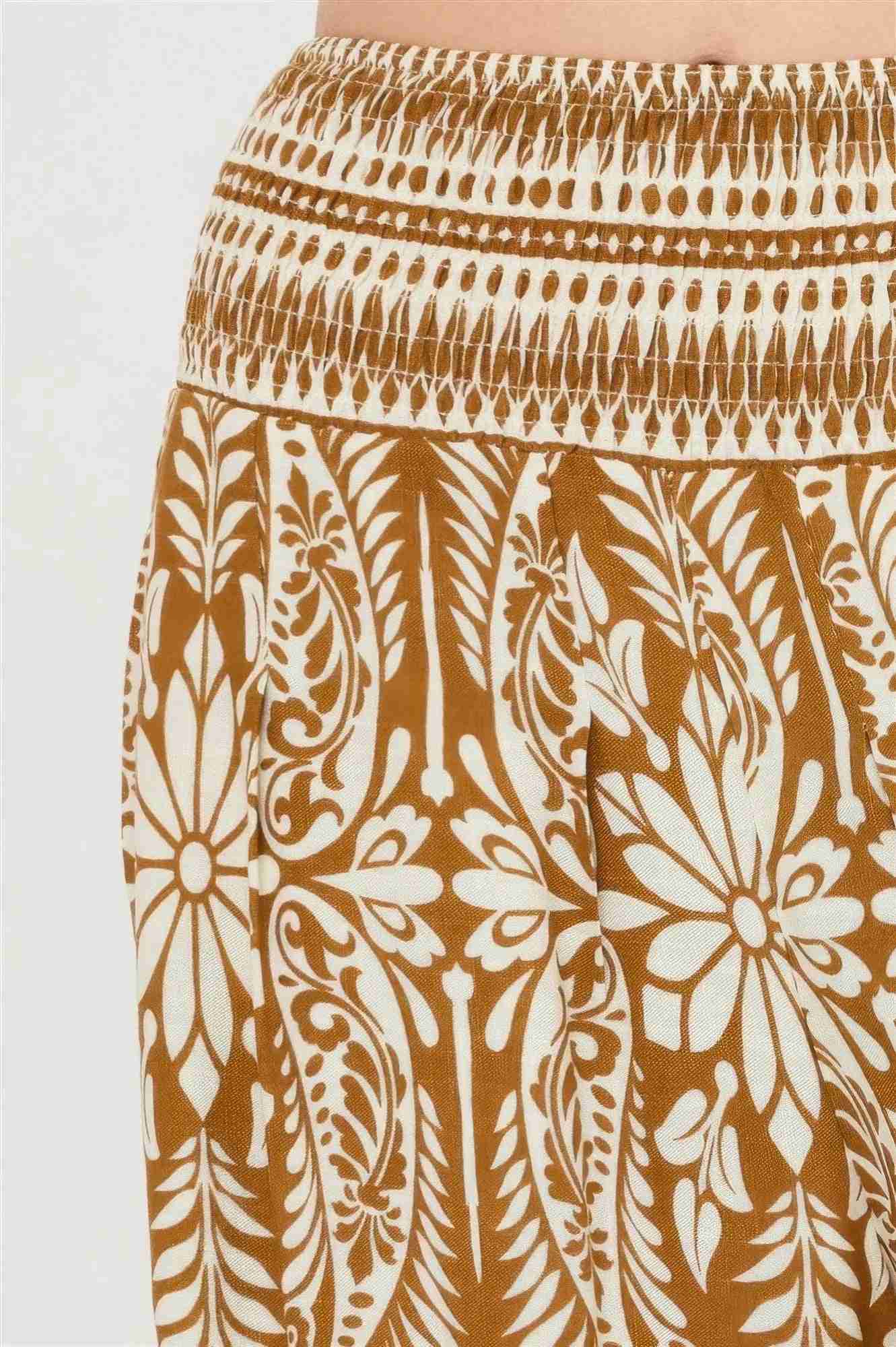 Pantalon ocre à motif floral blanc, détail du tissu avec imprimé décoratif.