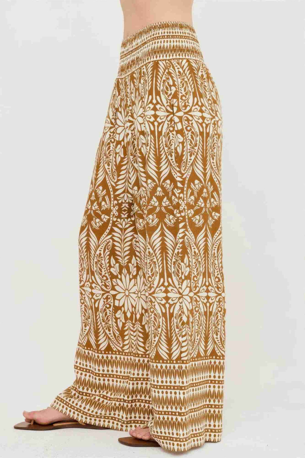 Pantalon long ample ocre à motif végétal blanc, taille smockée et ourlet rayé.