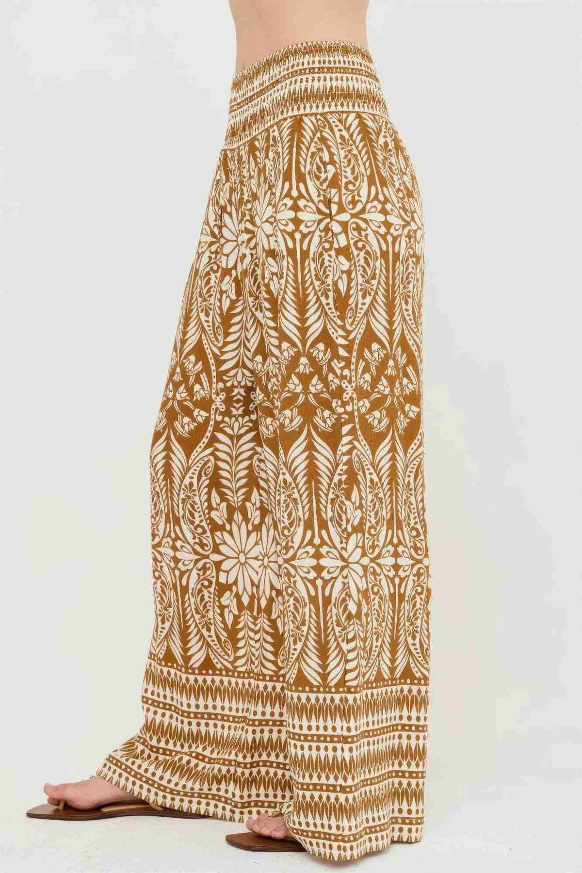 Pantalon long ample ocre à motif végétal blanc, taille smockée et ourlet rayé.