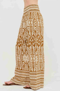 Pantalon long ample ocre à motif végétal blanc, taille smockée et ourlet rayé.