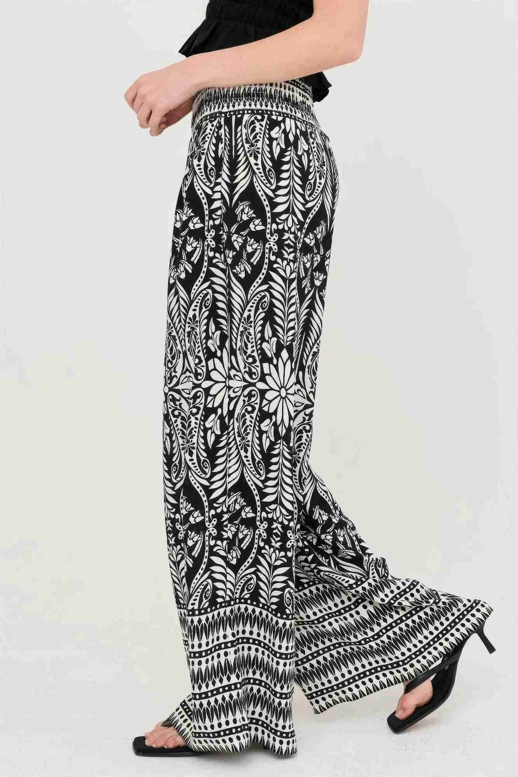 Pantalon fluide noir à motifs floraux blancs, taille smockée, bas évasé et volanté.