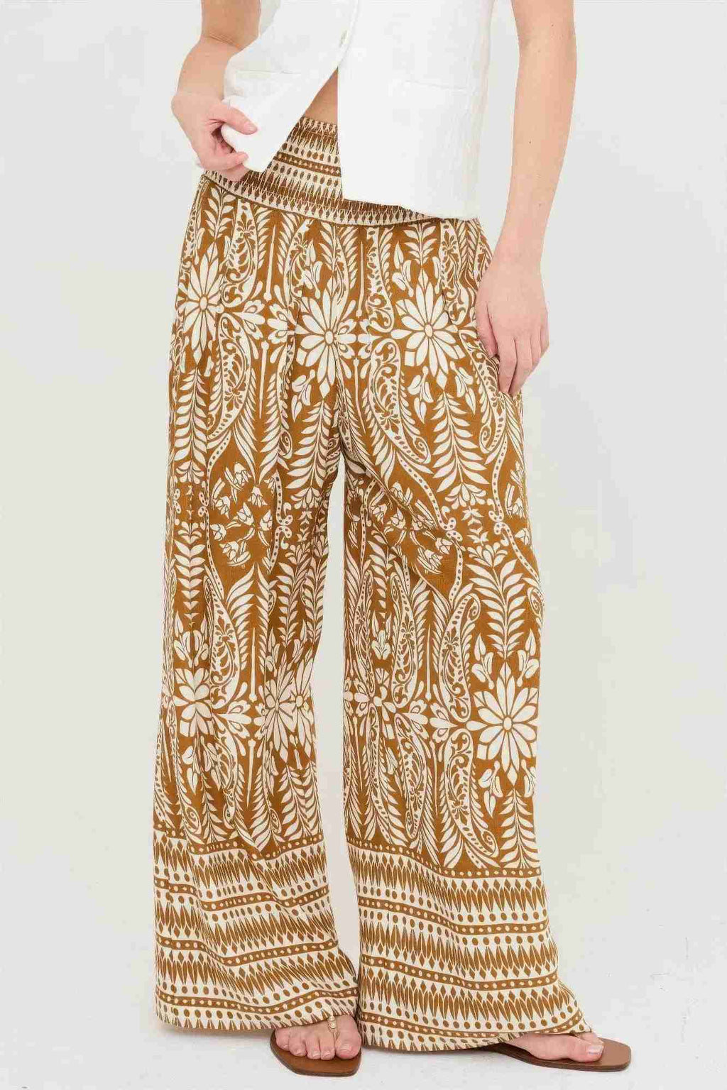 Pantalon ample ocre à motifs fleuris blancs, taille smockée, jambes longues évasées.