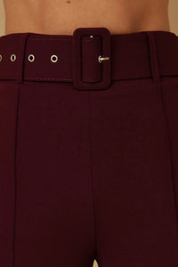 Détail pantalon bordeaux : ceinture à boucle carrée et œillets sur le passants