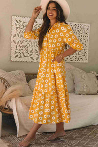 Robe maxi jaune à fleurs blanches, col chemisier, manches trois-quarts, boutons visibles.
