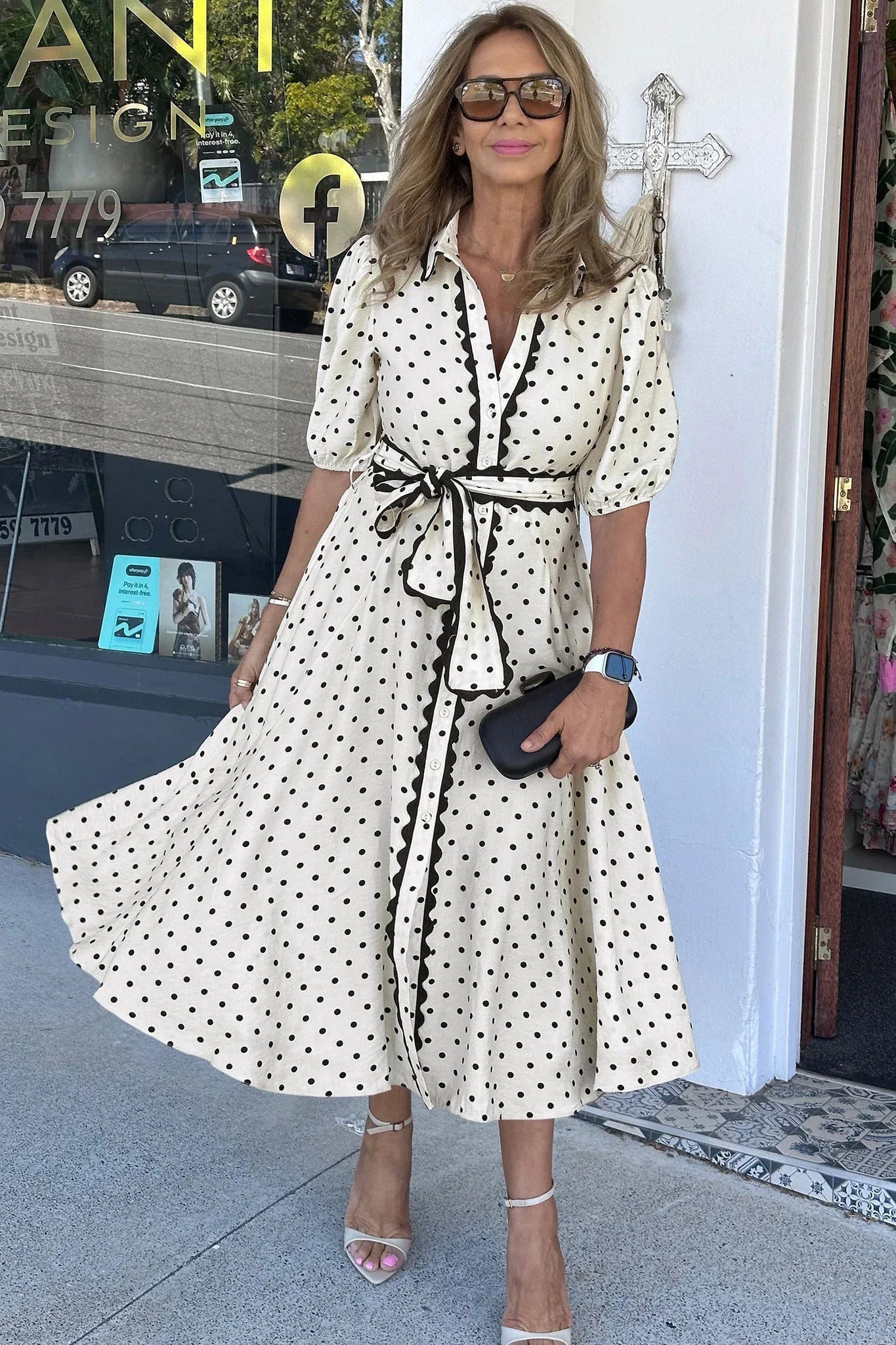 Robe midi blanche à pois noirs, col chemise et ceinture nouée, ourlet évasé.