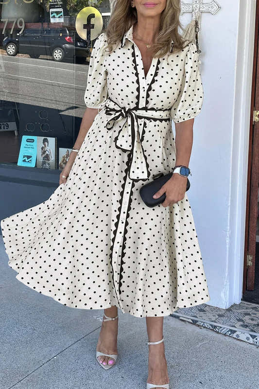 Robe midi blanche à pois noirs, col chemise et ceinture nouée, manches trois-quarts.