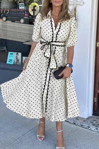Robe midi blanche à pois noirs, col chemise et ceinture nouée, manches trois-quarts.