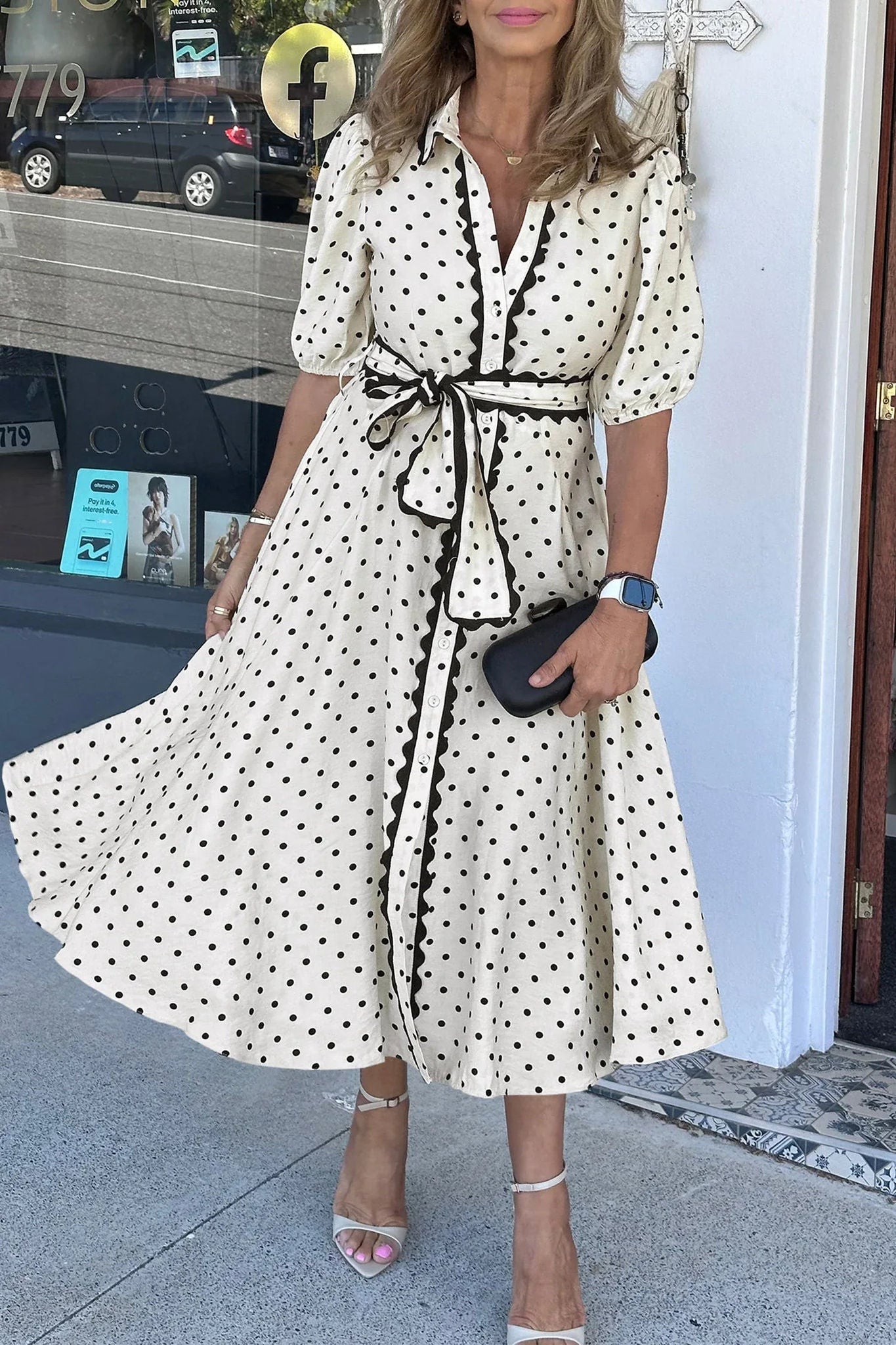 Robe midi blanche à pois noirs, col chemise et ceinture nouée, manches trois-quarts.