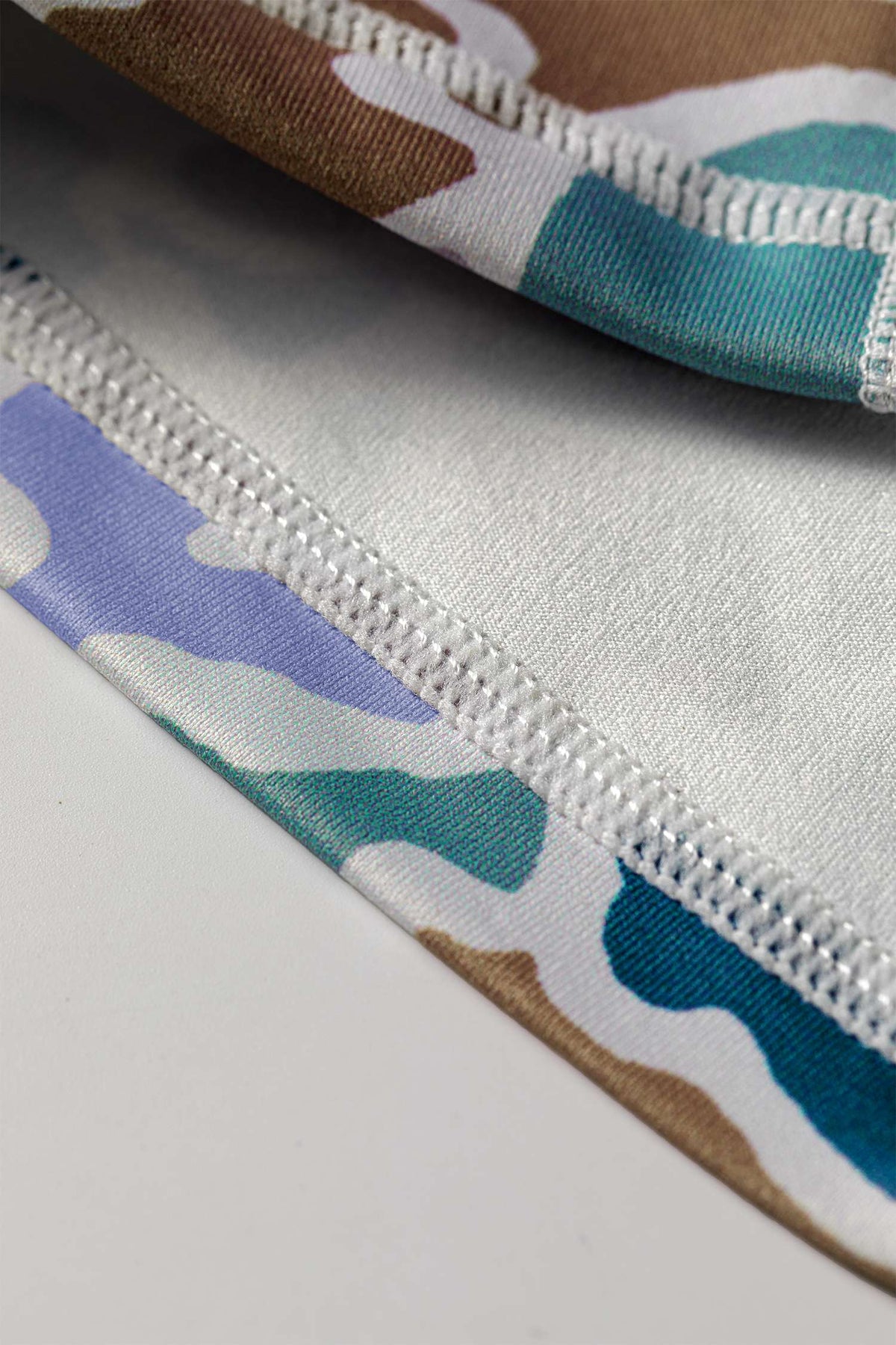 Couture d’ourlet et élastique blanc sur short cycliste imprimé camouflage multicolore.